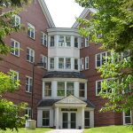 A brick building with large windows and a central entrance labeled ALFOND, surrounded by trees.