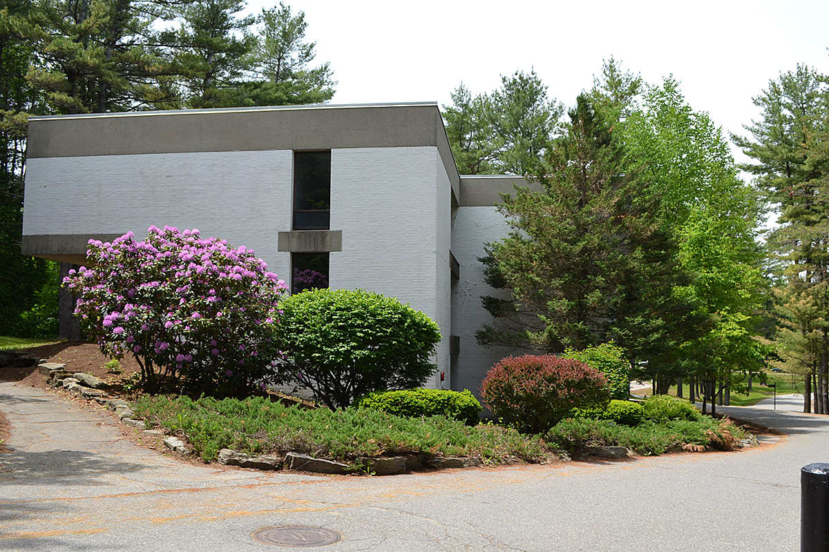 A modern building surrounded by lush greenery and blooming flowers on a sunny day in a serene setting.