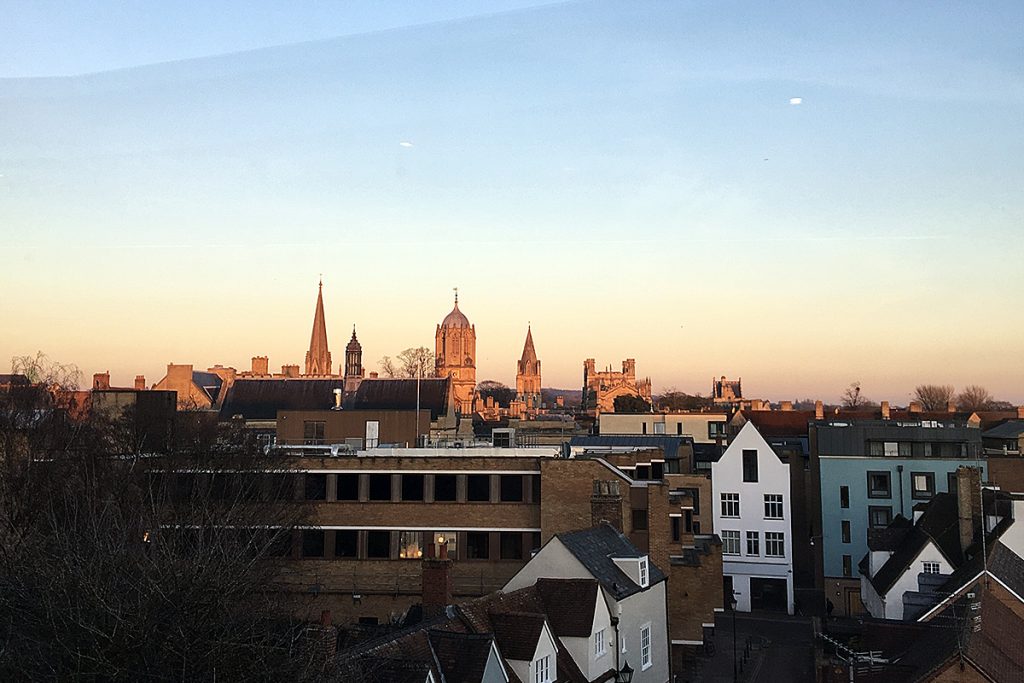 Sunset over a city skyline featuring church spires and historic buildings against a colorful sky.