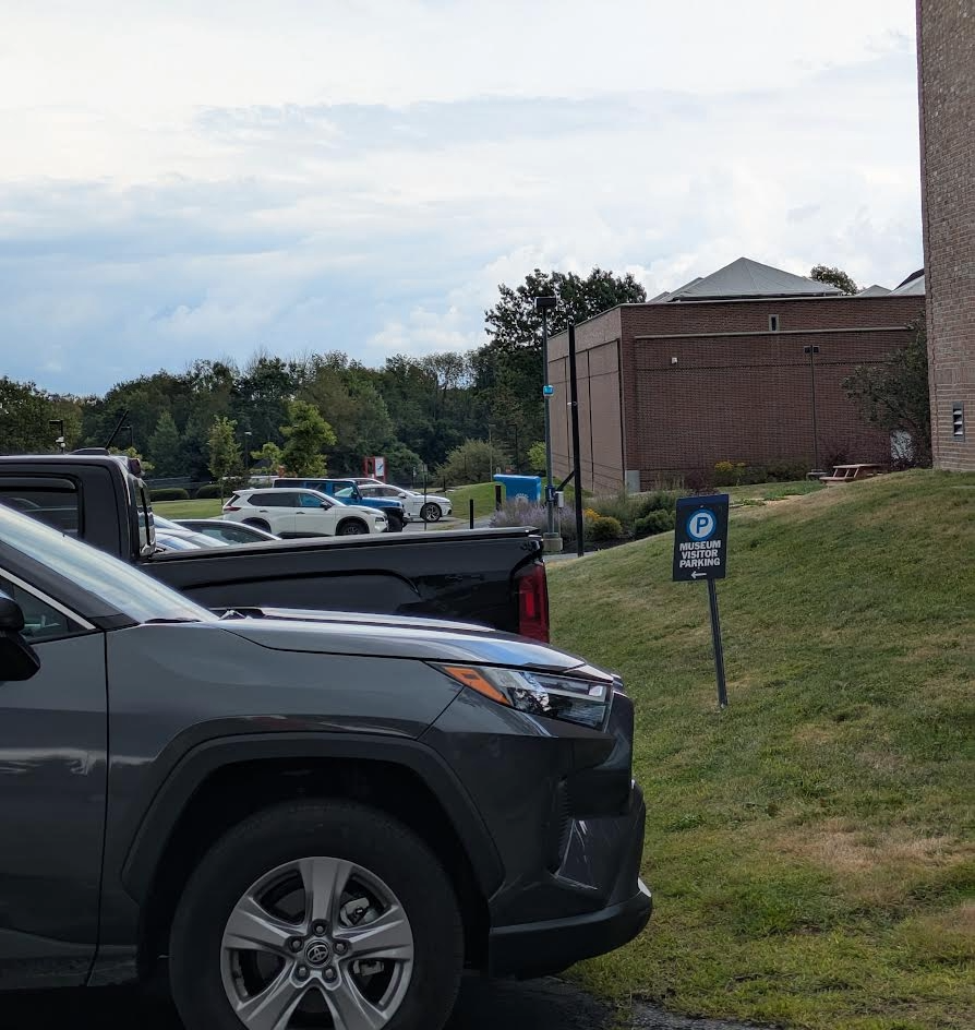 Gray vehicle parked near a building, with a sign indicating parking regulations partially visible in the background.