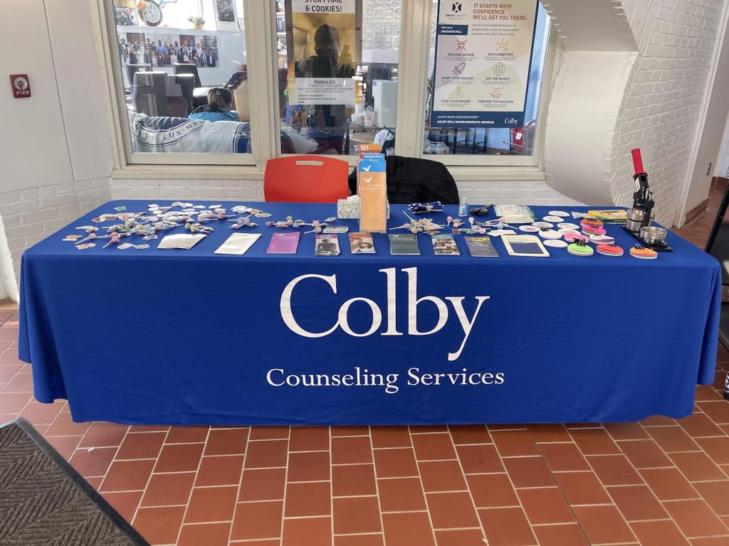 Table with Colby Counseling Services banner, displaying pamphlets, stickers, and promotional items.