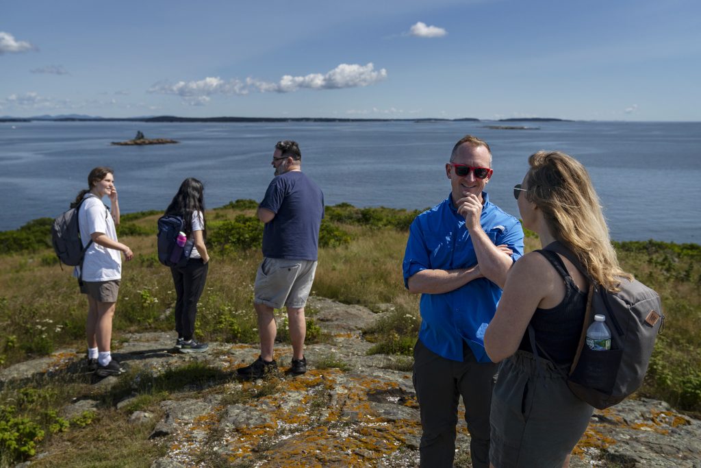 Group of five people enjoying a scenic view by the water, with some standing and others engaged in conversation.
