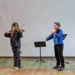 Two people in a studio playing violin